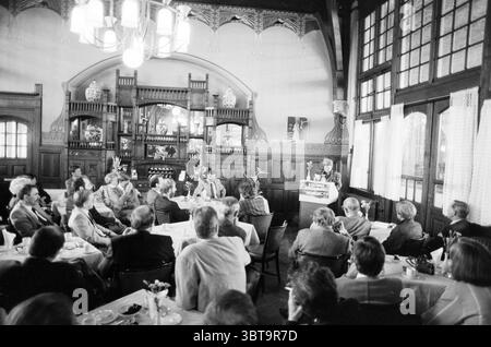 Eröffnung der Station Haarlem Eröffnung der Öffnungen Inbetriebnahme Station Haarlem Niederlande, Whizgle News, Dutch Desk, Niederlande, 1950 - 2000 am 11-05-1989. Diese Themen sind in der Abbildung dargestellt. Die Szene entfaltet sich in einem elegant dekorierten Speisesaal, der von hohen Holzbalken und kunstvollen Details geprägt ist, die einen Sinn für historischen Charme widerspiegeln. Die Wände sind mit komplizierten Mustern verziert, während große Fenster natürliches Licht eindringen lassen und trotz der monochromatischen Töne der Umgebung ein weiches, warmes Ambiente schaffen. Im Vordergrund steht ein Sprecher auf einem einfachen Podium und spricht an Stockfoto
