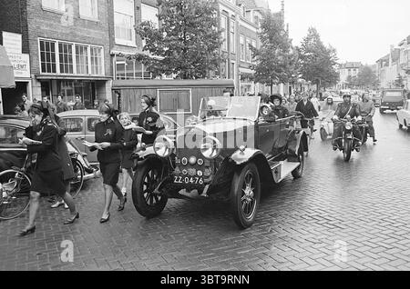 Heeresarmee Parade Parades, Whizgle News, Dutch Desk, Niederlande, 1950 - 2000 am 30-09-1967. Das Bild enthält diese Themen. In einer belebten urbanen Straßenszene hebt sich ein Oldtimer aus den 1920er Jahren deutlich hervor. Das Fahrzeug mit seinem glänzend dunklen Äußeren besticht durch elegante Kurven und ein klassisches Design, komplett mit einem glänzenden Frontgrill und großen Rädern. Das Cabrioverdeck ist unten und deutet auf eine lässige, feierliche Atmosphäre hin. Um das Fahrzeug herum geht eine Gruppe von Menschen mit lebhafter Energie zusammen. Sie sind in Vintage-Kleidung gekleidet, die für diese Zeit charakteristisch ist, mit Frauen in Röcken und Stockfoto