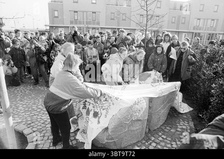 Enthüllung der Statue Toolenburg Hoofddorp the Netherlands, Whizgle News, Dutch Desk, Niederlande, 1950 - 2000 am 07-03-1993. Dies sind die Elemente im Bild. In einer lebhaften Outdoor-Szene versammelt sich eine Gruppe von Kindern und Erwachsenen um eine große Steinskulptur in einem Landschaftsbereich. Die Menge ist animiert, mit Ausdrücken der Neugier und Begeisterung, die sich auf ihren Gesichtern widerspiegeln. Nach vorne ziehen mehrere Kinder ein großes, farbenfrohes Tuch zurück, das die Skulptur darunter verbirgt. Ihre Kleidung ist mehrlagig, was auf eine kühle Umgebung hindeutet, mit lebhaftem ja Stockfoto