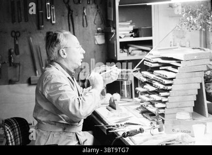 Orgelfabrik von. Füllfederhalter Utrecht Fabriken Herstellung Studios Orgeln und Organisten Utrecht, Whizgle News, Dutch Desk, Niederlande, 1950 - 2000 am 08-12-1983. Die Abbildung zeigt diese Themen. In einer gemütlichen Werkstatt mit dem warmen Ambiente von Holz und Handwerkskunst sitzt ein älterer Mann auf einer Holzwerkbank, die mit Werkzeugen und Materialien übersät ist. Er trägt eine helle, etwas getragene Schürze über einem geknöpften Hemd, was seine Hingabe an sein Handwerk beweist. Sein Haar ist grau und leicht zerzaust, was darauf hindeutet, dass er schon seit einiger Zeit in seine Arbeit vertieft ist. Die Lichtquelle überhitzt Stockfoto