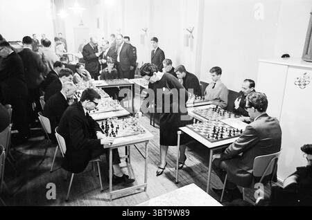 Fünf Damen vom Hoogoven Chess Tournament - Leser IJmuider Courant Chess, Whizgle News, Dutch Desk, Niederlande, 1950 - 2000 am 22.01.1965. Dies sind die Elemente im Bild. In einer belebten Halle findet ein Schachturnier statt. Der Raum ist mit einer Mischung von Menschen gefüllt, überwiegend Männern, die an verschiedenen Tischen sitzen und konzentriert über Schachbrettern sitzen. Jeder Tisch enthält eine Reihe von Schachfiguren, einige in strategischer Form, während andere in der Mitte des Spiels sind. Die Spieler sind in einer Vielzahl von Stilen gekleidet, von formellen Anzügen bis hin zu lässigeren Kleidungsstücken, die eine Mischung aus Epochen widerspiegeln Stockfoto