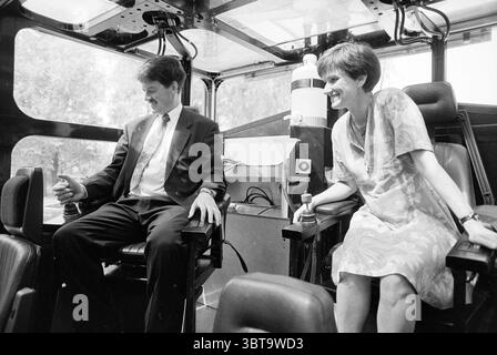 Lord van Gils mit der neuen Polizeiwasserkanone Haarlem the Netherlands, Whizgle News, Dutch Desk, Niederlande, 1950 - 2000 am 20.05.1992. Die Abbildung zeigt diese Themen. Die Szene zeigt einen geräumigen Innenraum, wahrscheinlich ein Fahrzeug oder ein spezielles Fach, das sich durch ein modernes Design und eine funktionale Anordnung auszeichnet. Zwei Personen stehen im Vordergrund: Ein Mann und eine Frau, beide sitzen bequem, aber mit unterschiedlichen Haltungen, die ihre Auseinandersetzung mit der Umgebung widerspiegeln. Der Mann, gekleidet in einem knackigen Anzug, wirkt entspannt, aber aufmerksam, lehnt sich leicht nach vorne mit einem subtilen Lächeln und schlägt ein s vor Stockfoto