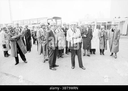Gruppe von Personen auf dem Parkplatz der Busse, Whizgle News, Dutch Desk, Niederlande, 1950 - 2000 am 02-11-1989. Diese Themen werden in der Abbildung angezeigt. Die Szene zeigt eine Gruppe von Männern und Frauen, die sich im Freien versammelt haben und sich hauptsächlich mit Gesprächen beschäftigen. Die Einzelpersonen tragen formelle Kleidung und viele tragen lange Mäntel, die auf eine professionelle Umgebung oder Veranstaltung hinweisen. Die meisten Männer tragen Anzüge und viele sind mit Hüten verziert, die ihrem Aussehen einen klassischen Touch verleihen. Die Farbpalette ist gedämpft und besteht hauptsächlich aus Grautönen, Schwarztönen und Beigetönen, was der Szene ein düsteres und für verleiht Stockfoto