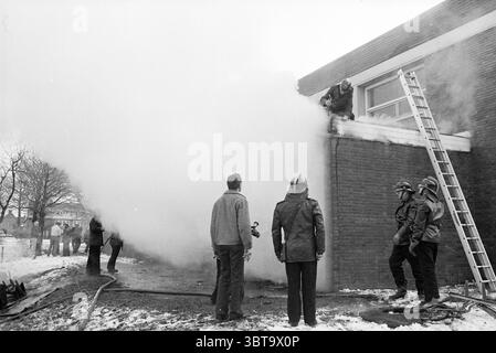 Fire Houtmanpad Fire Brigade Haarlem Houtmanpad Niederlande, Whizgle News, Dutch Desk, Niederlande, 1950 - 2000 am 23-12-1982. Dies sind die Elemente im Bild. Die Szene fängt einen dramatischen Moment eines Brandfalls ein, der sich in einer düsteren, urbanen Umgebung entfaltet. Eine schwere Rauchwolke weht aus einem Gebäude, umhüllt die Luft in ein dickes, graues Tuch und verdeckt den Blick auf das Innere. Im Vordergrund steht eine kleine Gruppe von Zuschauern, deren Ausdruck eine Mischung aus Besorgnis und Neugier widerspiegelt. Sie tragen legere Kleidung und stehen im Kontrast zu den Uniformen des Feuerwehrmanns Stockfoto