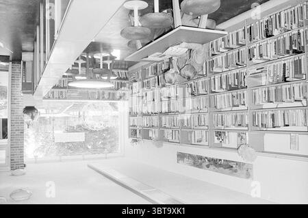 Geschäfte von. Zeggelenplein Interior Haarlem Van Zeggelenplein The Netherlands, Whizgle News, Dutch Desk, Niederlande, 1950 - 2000 am 28-09-1973. Das Bild enthält diese Themen. Die Szene zeigt eine moderne Bibliothek oder einen Arbeitsbereich mit einer klaren, minimalistischen Ästhetik. Die Wände sind mit Regalen gefüllt mit einer Vielzahl von Büchern, deren Rücken in verschiedenen Farben und Größen zeigen, was ein Gefühl der Organisation in der Fülle des Wissens verleiht. Diese Regale sind zielgerichtet angeordnet und tragen zu einer strukturierten Atmosphäre des Raumes bei. Im Vordergrund sitzen zwei Individuen in einem slee Stockfoto