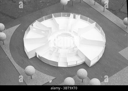 Modellkindergarten im Maßstab. Modellmaßstab, Whizgle News, Dutch Desk, Niederlande, 1950 - 2000 am 25-08-1970. Dies sind die Themen im Bild. Die Szene zeigt ein kreisförmiges Architekturmodell auf einer strukturierten Oberfläche, umgeben von einer ruhigen Landschaft. Die Struktur besteht aus stark weißen Materialien und zeigt eine Reihe geometrischer Formen, die von einem zentralen kreisförmigen Kern ausstrahlen. Mehrere Trennwände schaffen unterschiedliche, miteinander verbundene Räume innerhalb des Modells, was auf eine durchdachte Organisation der Bereiche hindeutet. Die Landschaftsgestaltung verfügt über minimalistische, gleichmäßig verteilte sphärische Formen, die ähneln Stockfoto
