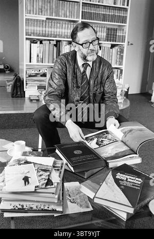 Porträt von Professor Stuart Verrijn in Haarlem Personen Haarlem Niederlande, Whizgle News, Dutch Desk, Niederlande, 1950 - 2000 am 01-04-1982. Das Bild enthält diese Themen. Die Szene zeigt einen gut gekleideten Mann, der in einem gemütlichen, mit Büchern gefüllten Raum sitzt. Er trägt einen dunklen Blazer über einem weißen Hemd und eine Krawatte, die einen Hauch von Kontrast verleiht. Seine Brille ist sehr Retro und ergänzt sein wissenschaftliches Aussehen. Vor ihm steht ein großes Buch offen, das atemberaubende Bilder von Bergen enthüllt, die auf ein Thema der Erkundung oder des Abenteuers hinweisen. Um ihn herum sind Stapel verschiedener Bücher A Stockfoto