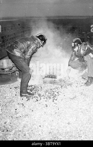 Feuerwehrwohnung Schalkwijk Fire Brigade, Whizgle News, Dutch Desk, Niederlande, 1950 - 2000 am 21-01-1972. Dies sind die Themen im Bild. Die Szene fängt zwei Figuren in einer dramatischen, hoch gelegenen Umgebung ein, umgeben von einem Nebel aus Rauch, der von einem kleinen Feuer auf einem Dach aufsteigt. Beide Personen tragen dunkle, schwere Lederjacken und tragen Helme, die ihr Gesicht verdecken und dem Moment einen Hauch von Mysterium und Intensität verleihen. Die Kulisse bietet einen weitläufigen Blick auf die Stadtlandschaft, die Gebäude erscheinen als Silhouetten vor einem verblassten Himmel. Die Atmosphäre ist voller Rauch Stockfoto