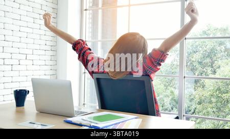 Frau streckt den Arm hoch und sitzt falsch in der Position des Home Office-Schreibtisches. Rückseite einer jungen asiatischen Frau müde von der Arbeit Körper Stress Rücken Schmerz Büro Sy Stockfoto