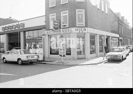 Erw. Jugendzentrum d'Appelaer extern. Jugendzentrum Kampersingel ext. Garage Amsterdamsevaart Exterior Haarlem Kampersingel Niederlande, Whizgle News, Dutch Desk, Niederlande, 1950 - 2000 am 22-03-1972. Diese Themen werden in der Abbildung angezeigt. Die Szene zeigt eine charmante Straßenecke in Schwarz-weiß-Ästhetik, die eine nostalgische Atmosphäre weckt. Auf der linken Seite befindet sich eine gut gepflegte Tankstelle mit einem schlanken, modernen Design mit großen Fenstern und einem markanten Schild, das die Marke unterstreicht. Die leicht abgenutzten und dennoch funktionalen Gaspumpen deuten auf ein hektisches Leben hin. Direkt auf der anderen Straßenseite befindet sich ein Auto Stockfoto