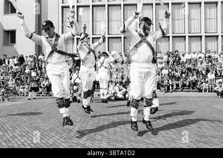 Morris-Tänzer in IJm. Dancing, Whizgle News, Dutch Desk, Niederlande, 1950 - 2000 am 03-09-1977. Das Bild enthält diese Themen. In der Szene wird eine Gruppe von fünf Männern in einem lebhaften traditionellen Tanz engagiert, deren Bewegungen energetisch und synchronisiert sind. Sie tragen weiße Hosen und Hemden und tragen schwarze Westen mit dekorativen Gürteln, die einen auffälligen Kontrast zu ihren Outfits bilden. Jede Tänzerin trägt eine schwarze Kappe, die die Gleichmäßigkeit ihres Aussehens erhöht. Die Tänzer werden mitten im Sprung mit hochgezogenen Armen gefangen, wodurch ein Eindruck von Freude und Feier entsteht. Die Mo Stockfoto