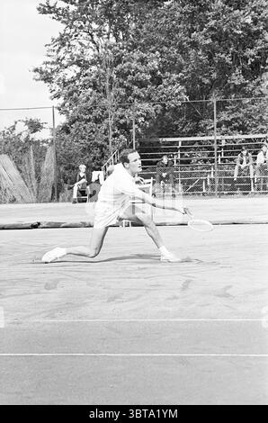 Tennis Brederode III Jaidip Mukerjea-Tom Okker Santpoort, Whizgle News, Dutch Desk, Niederlande, 1950 - 2000 auf 30-07-1965. Dies sind die Elemente im Bild. In einer lebhaften Outdoor-Umgebung wird ein Tennisspieler mitten in der Action auf einem Sandplatz gefangen. Er trägt ein klassisches weißes Tennis-Outfit, das ein kurzärmeliges Hemd und Shorts umfasst und den sportlichen Aufbau seiner Form zeigt, während er sich dramatisch vorwärts springt. Der Spieler hält einen Schläger in der rechten Hand, der für einen kräftigen Schlag bereit ist. Sein Gesicht zeigt Konzentration und Entschlossenheit. Um den Hof herum, eine Kulisse aus üppigem Grün Stockfoto