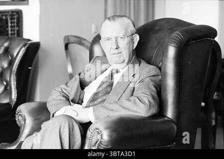 Rev. IJzerman Haarlem Pastor Haarlem The Netherlands, Whizgle News, Dutch Desk, Niederlande, 1950 - 2000 am 20-04-1984. Das Bild enthält diese Themen. In einem gemütlichen, sanft beleuchteten Raum sitzt ein älterer Herr bequem in einem großen, dunklen Ledersessel, der eine elegante, zeitlose Qualität hat. Der Stuhl ist reich strukturiert, mit tiefen Kurven und polierten Armen, die sowohl Komfort als auch Raffinesse vermitteln. Der Mann, der in einem maßgeschneiderten grauen Anzug gekleidet ist, hat ein dezentes Karomuster, das einen klassischen Stil angibt. Seine Krawatte hat einen warmen, aber kontrastierenden Farbton, der einen Hauch von Charakter in der Mitte des M verleiht Stockfoto