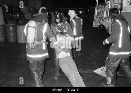 Feuerwehrübung Pijpkade Beverwijk Feuerwehr Beverwijk Nederland, Whizgle News, Dutch Desk, Niederlande, 1950 - 2000 am 22-11-1983. Die Abbildung zeigt diese Themen. In einer dramatischen und angespannten Szene trägt eine Gruppe von Personen, wahrscheinlich Notfallhelfern, dunkle, schwere Mäntel mit reflektierenden Streifen, die das Licht einfangen und ihre Sichtbarkeit gegenüber der dunklen Umgebung verbessern. Ihre Äußerungen sind ernst, sie vermitteln Dringlichkeit und Konzentration, da sie mitten in einer Rettungsaktion zu sein scheinen. In der Mitte der Szene wird ein Responder gesehen, der eine andere Person trägt, W Stockfoto