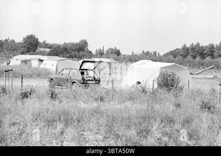 Verschiedene Strand- und Campingfotos IJmuiden und Spaarnwoude Camping Strand und Strände IJmuiden Niederlande, Whizgle News, Dutch Desk, Niederlande, 1950 - 2000 auf 24-07-1983. Das Bild enthält diese Themen. Die Szene zeigt einen Campingplatz in einer weiten, offenen Landschaft. Es gibt eine Vielzahl von Zelten, meist in gedämpften Farben wie Beige und weiß, die sich subtil in die natürliche Umgebung einfügen. Diese Zelte sind leicht verstreut auf einem grasbewachsenen Feld angeordnet, was auf eine ungezwungene und informelle Zelteinrichtung hindeutet. Im Vordergrund steht ein kleiner Wagen neben einem der Zelte. I Stockfoto