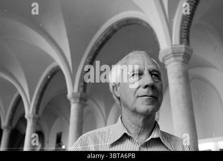 Künstler mr. Grabijn Rathaus Refektorium, Whizgle News, Dutch Desk, Niederlande, 1950 - 2000 am 03-08-1995. Diese Themen sind in der Abbildung dargestellt. In einer monochromatischen Szene steht ein Mann in einer weitläufigen, architektonischen Umgebung, die von hohen, anmutigen Bögen geprägt ist, die den Blick nach oben ziehen. Die Bögen aus Stein weisen ein klassisches Design auf und erzeugen einen Rhythmus, der der Umgebung ein Gefühl von Pracht verleiht. Der Ausdruck des Mannes ist nachdenklich, mit einer leichten Furche in der Stirn. Er trägt ein helles gestreiftes Hemd, das sich sanft mit den dunkleren Tönen des Hintergrunds abhebt. Sein Ha Stockfoto