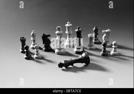 Chess Pieces., Whizgle News, Dutch Desk, Niederlande, 1950 - 2000. Diese Themen werden in der Abbildung angezeigt. Die Szene zeigt eine Sammlung von Schachstücken, die dynamisch und dennoch chaotisch auf einer glatten Oberfläche angeordnet sind. Die Stücke sind überwiegend weiß und schwarz und zeigen einen klassischen Kontrast. Mehrere Figuren stehen aufrecht, darunter Ritter, Bäche, Bischöfe und Bauern. jedes Detail mit unterschiedlichen Formen und Größen, die ihre einzigartige Rolle im Spiel widerspiegeln. Die Beleuchtung ist weich und gestreut und erzeugt sanfte Schatten, die der Szene Tiefe und Dimension verleihen. Der Hintergrund ist Stockfoto