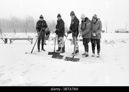 Schaufel Schneeisbahn IJmuiden Schneeisbahn Eishockey IJmuiden Niederlande, Whizgle News, Dutch Desk, Niederlande, 1950 - 2000 am 08-01-1985. Dies sind die Elemente im Bild. Die Szene zeigt eine Gruppe von sechs Individuen, die auf einer schneebedeckten Oberfläche stehen und mit der Aufgabe beschäftigt sind, Schnee zu schaufeln. Sie sind in Winterkleidung gekleidet, was auf eine kalte Umgebung hindeutet, mit Materialien wie schweren Mänteln, Hüten und Tüchern in neutralen und dunkleren Farben, die mit dem hellen weiß des Schnees kontrastieren. Die Einzelpersonen sind in einer losen Linie angeordnet, jeder hält eine Schaufel, mit ihren Pos. Stockfoto