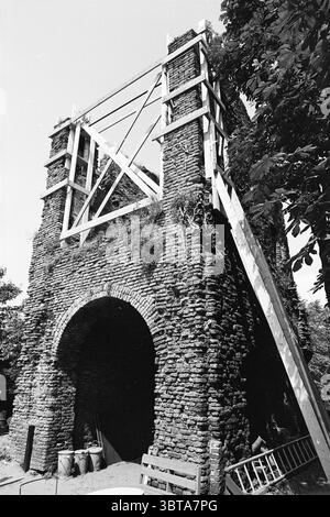 Ruin of Brederode in Gerüstruin, Whizgle News, Dutch Desk, Niederlande, 1950 - 2000 am 23-06-1981. Dies sind die Elemente im Bild. Die Szene zeigt eine hohe, teilweise gebaute Steinstruktur mit einer rauen, strukturierten Fassade aus dunklen Steinen. Das Gebäude scheint einen bogenförmigen Eingang zu haben, der die Zuschauer einlädt, hineinzuschauen. Um den Torbogen herum sind die Steine ungleichmäßig geformt, was zu einem rustikalen Charme beiträgt. Oberhalb des Bogens stehen Holzgerüste im Kontrast zum Stein und unterstützen die laufenden Bauarbeiten. Der Rahmen besteht aus hellen Strahlen, Form Stockfoto