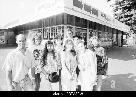 Mitarbeiter der Firma KOM + Koop, Whizgle News, Dutch Desk, Niederlande, 1950 - 2000 am 26-05-1992. Dies sind die Elemente im Bild. Die Szene zeigt eine Gruppe von neun Individuen, die sich auf einer gepflasterten Fläche vor einer modernen, hellen Ladenfront mit einer markanten Markise versammelt haben. Das Gebäude hat ein elegantes, kommerzielles Aussehen, das von großen Fenstern unterstrichen wird, die einen Blick auf das Innere freigeben. Im Vordergrund sind die Menschen eng zusammengestellt, lächeln und vermitteln ein Gefühl von Kameradschaft. Ihre Kleidung spiegelt eine Mischung aus Stilen wider, von lässig bis etwas eleganter und in hellen Farben Stockfoto