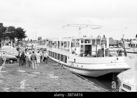 Kreuzfahrt für Behinderte Lisserbroek Kreuzfahrt Sightseeing-Touren Sightseeing-Flüge Lisserbroek, Whizgle News, Dutch Desk, Niederlande, 1950 - 2000 am 23-09-1989. Dies sind die Elemente im Bild. Die Szene zeigt eine lebhafte Uferpromenade mit einem großen weißen Passagierboot, das nebenan angedockt ist. Das Boot mit seinem markanten Oberdeck und zahlreichen Fenstern scheint vor Aktivität zu strotzen, da sich mehrere Personen an seinen Seiten versammeln und sich wahrscheinlich auf ein- oder Aussteigen vorbereiten. Im Vordergrund steht eine Menge verschiedener Menschen auf dem Gras, von denen einige animiert plaudern, während andere wie wartend wirken Stockfoto