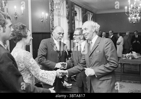 HR. Jubiläum und Empfang Kalf Haarlems Dagblad etc. Und IJmuider Courant and Koeri, Whizgle News, Dutch Desk, Niederlande, 1950 - 2000 am 15.09.1970. Dies sind die Themen im Bild. In einem gut beleuchteten Innenraum gibt es in formeller Kleidung einen herzlichen Handschlag. Die Szene umfasst eine Vielzahl von Menschen, einige tragen dunkle Anzüge und andere entscheiden sich für hellere Farben, was der Komposition einen Kontrast verleiht. Ein besonderes Merkmal ist die elegante Einrichtung des Zimmers, die durch Holztäfelung und kunstvolle Kronleuchter gekennzeichnet ist, die ein warmes, einladendes Leuchten erzeugen. Die Wände sind mit r Stockfoto