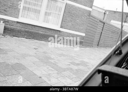 Bienenschwarm im Baum Leidsevaart Bienen Haarlem Leidsevaart Niederlande, Whizgle News, Dutch Desk, Niederlande, 1950 - 2000 am 17-08-1987. Diese Themen sind in der Abbildung dargestellt. Die Szene bietet einen Blick auf einen teilweise geschlossenen Außenbereich, der von Ziegelwänden geprägt ist, die ein Gefühl von Einsamkeit schaffen. Der Boden ist mit quadratischen Steinpflastern angelegt, die ordentlich angeordnet sind, was auf einen gepflegten Raum hindeutet. Im Vordergrund ist ein Teil eines Fahrzeugs zu sehen, was auf einen gelegentlichen oder alltäglichen Kontext hindeutet. Seine Winkel und Konturen treten dezent aus dem unteren Rand hervor und stehen im Kontrast zum strukturierten lin Stockfoto