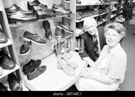 Herr und Frau Van Doorn ADO Schuhgeschäft, Whizgle News, Dutch Desk, Niederlande, 1950 - 2000 am 03-05-1995. Dies sind die Elemente im Bild. Die Szene zeigt eine gut organisierte Ausstellung von Schuhen, die ordentlich in Regalen angeordnet sind. Die Schuhe umfassen verschiedene Stile, wie z. B. Kleiderschuhe, Freizeitschuhe und sportliche Optionen, in denen eine Reihe von Farben, darunter klassische Schwarz-, Braun- und hellere Farbtöne, präsentiert werden. Im Vordergrund sitzen zwei Personen an einem kleinen Tisch. Eine Person, ein Mann, trägt einen dunklen, gemusterten Anzug mit einer Krawatte, die ein lebhaftes Design hat und seinem A einen Farbakzent verleiht Stockfoto