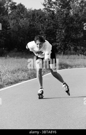 Rollschuhlaufen, Whizgle News, Dutch Desk, Niederlande, 1950 - 2000 im Jahr 1991. Diese Themen sind in der Abbildung dargestellt. In einer Szene, in der eine Person schnell auf einem glatten, gewundenen Pfad gleitet, liegt der Fokus auf der dynamischen Bewegung und dem sportlichen Verhalten. Die Person, die in einem hellen kurzärmeligen Hemd und dunklen Shorts gekleidet ist, scheint tief konzentriert zu sein, lehnt sich leicht nach vorne, wobei das eine Bein ausgestreckt und das andere hinter sich zurückgezogen ist, was auf einen kräftigen Push-off hindeutet. Die Umgebung ist von einer üppigen Grünfläche umgeben, mit hohen Bäumen, die den Weg säumen, deren Blätter vor ihnen lebendig sind Stockfoto