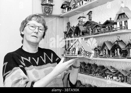 Frau Wittekoek Weather Houses, Whizgle News, Dutch Desk, Niederlande, 1950 - 2000 am 13-12-1993. Dies sind die Themen im Bild. In einem gemütlichen Innenraum steht eine Frau im Vordergrund, die ein dekoratives Holzhausmodell hält. Sie trägt eine runde Brille und einen stylischen Pullover mit einem auffälligen geometrischen Muster, überwiegend in Grautönen mit Kontrastfarben. Die Atmosphäre ist warm und einladend, was auf eine Leidenschaft zum Basteln oder Sammeln hindeutet. Hinter ihr befinden sich eine Reihe von Regalen mit einer Reihe von aufwendig gestalteten Miniaturhäusern, die leuchtende Farben A zeigen Stockfoto