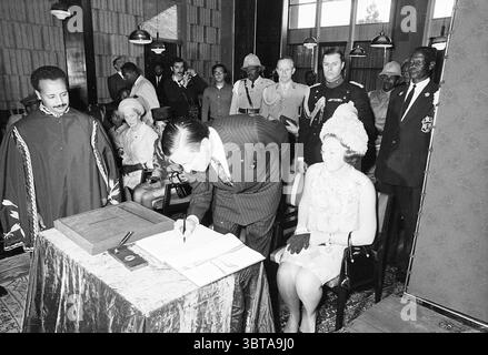Königin Juliana Prinz Bernhard Prinzessin Beatrix Prinz Claus und Delegation bei Staatsbesuch in Äthiopien (Jan - Feb) Ethiopië, Whizgle News, Dutch Desk, Niederlande, 1950 - 2000 1969. Das Bild enthält diese Themen. In einer formalen Inneneinrichtung, die von einer Mischung aus historischer und politischer Bedeutung geprägt ist, entfaltet sich ein bedeutender Moment. Der Raum verfügt über eine strukturierte Holztäfelung und einfache industrielle Leuchten, die von der Decke hängen und einen warmen Glanz im gesamten Raum erzeugen. In der Mitte ist ein Mann in einem dunklen Anzug mit Schreiben beschäftigt, der konzentriert erscheint, während er ein Dokument auf einem t unterzeichnet Stockfoto