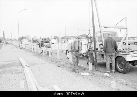 Guardrails Halfway Road Construction Road Planting, Whizgle News, Dutch Desk, Niederlande, 1950 - 2000 am 20-08-1968. Diese Themen sind in der Abbildung dargestellt. Die Szene fängt eine urbane Umgebung unter einem bewölkten Himmel ein und wirft ein weiches, diffuses Licht über die Gegend. Im Vordergrund ist eine Gruppe von Arbeitern an einem Bauprojekt beteiligt. Eine Person, die in schwerer Arbeitskleidung und Hut gekleidet ist, bedient ein Maschinenteil, das einem Bohrer oder einer Schnecke ähnelt und sich auf seine Aufgabe konzentriert. In der Nähe steht ein zweiter Arbeiter neben einem Lkw, der die Aktivität beobachtet und möglicherweise koordiniert. Die Landschaft bietet eine breite, Stockfoto