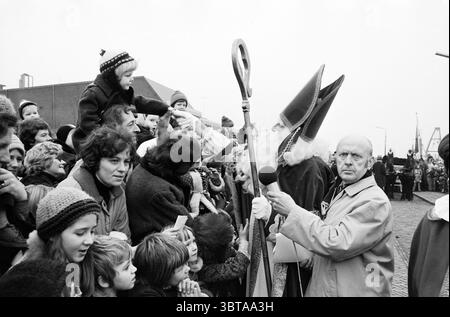 Saint Nicholas in IJmuiden - Heemskerk - Velsen-Noord St. Nicholas Sinterklaas, Whizgle News, Dutch Desk, Niederlande, 1950 - 2000 am 23-11-1974. Dies sind die Elemente im Bild. Die Szene entfaltet sich in einer hektischen Menge, gefüllt mit einer Mischung aus Erwachsenen und Kindern, die alle eifrig auf eine zentrale Figur zugreifen. Die Menschen zeigen eine Reihe von Ausdrucksformen, von Begeisterung und Vorfreude bis hin zu Neugier, deren Blick auf den Mittelpunkt gerichtet ist. Die Kinder, die warme Hüte und Mäntel tragen, wirken besonders animiert, manche strapazieren sich gegen ihre Eltern, um näher zu kommen. Die zentrale Figur, adorne Stockfoto