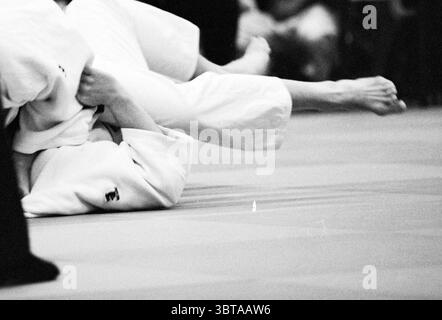 NK Judo Men Beverwijk Beverwijk the Netherlands, Whizgle News, Dutch Desk, Niederlande, 1950 - 2000 am 14-02-1997. Diese Themen sind in der Abbildung dargestellt. Die Szene fängt einen intensiven Moment in einem Judo-Match ein, bei dem der Fokus auf zwei Wettbewerbern liegt, die in einem dynamischen Kampf verwickelt sind. Die Athleten sind in traditionellem weißen Judo-Gi gekleidet, wobei einer von ihnen manövriert, um eine vorteilhafte Position zu erlangen. Im Vordergrund steht ein Teilnehmer, der teilweise überdreht ist und seine Beine unangenehm in der Luft positioniert sind. Die dezenten Details des Gi sind sichtbar, darunter die Falten des Materials und die Aufnäher Stockfoto