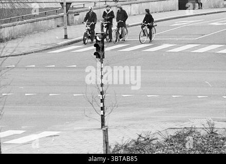 Besuchen Sie die Mendelcollege Schools Verkehrssicherheit, Whizgle News, Dutch Desk, Niederlande, 1950 - 2000 auf 30-11-1970. Diese Themen werden in der Abbildung angezeigt. Die Szene fängt einen Moment an einer Kreuzung mit einer Gruppe von vier Personen auf Fahrrädern ein. Sie stehen geduldig am Rande eines Querweges und warten auf ein Signal. Die Radfahrer tragen dunkle Kleidung und tragen einige Jacken, was auf einen kühleren Tag hindeuten könnte. Das städtische Umfeld ist von Asphaltstraßen geprägt, die durch weiße Fußgängerlinien auf dem Fußgängerübergang gekennzeichnet sind, die sich von der dunkleren Straßenoberfläche abheben. A Stockfoto