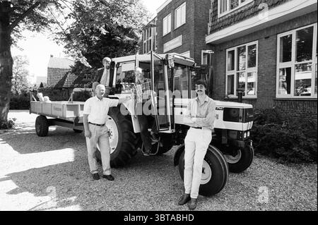 Neuer Traktor für landwirtschaftliche Schule Hoofddorp Schulen Hoofddorp Niederlande, Whizgle News, Dutch Desk, Niederlande, 1950 - 2000 am 13-06-1988. Das Bild enthält diese Themen. In dieser Szene versammelt sich eine Gruppe von vier Personen um einen großen, alten Traktor, der vor einem Backsteinhaus geparkt ist. Der Traktor, der gut positioniert ist, hat ein glänzendes weiß-schwarzes Äußere, das sein klassisches Design unterstreicht. Es hebt sich von den eher gedämpften Tönen der umgebenden Architektur ab. Die Einzelpersonen zeigen eine Reihe von Freizeitkleidung, mit drei Männern, die neben dem Traktor stehen, und einer Frau, die leani ist Stockfoto