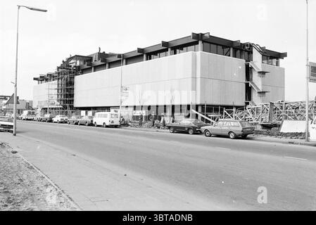 Externes Neubau Stoutenbeek Beverwijk Buildings Beverwijk, Whizgle News, Dutch Desk, Niederlande, 1950 - 2000 am 21-04-1978. Die Abbildung zeigt diese Themen. Die Szene zeigt eine befahrene Straße, die von einer sich entwickelnden Baustelle gesäumt wird. Auf der einen Seite nimmt ein modernes Gebäude Gestalt an, das sich durch seine scharfen Winkel und einen Materialmix aus Beton und Glas auszeichnet. Die Struktur zeigt eine minimalistische Ästhetik mit großen, leeren Wandpaneelen und einem scharfen, unfertigen Erscheinungsbild. Das Gerüst nimmt ein Ende ein, was auf laufende Arbeiten hindeutet, während eine Treppe schräg herausragt und Zugang zu höheren Gebäuden bietet Stockfoto