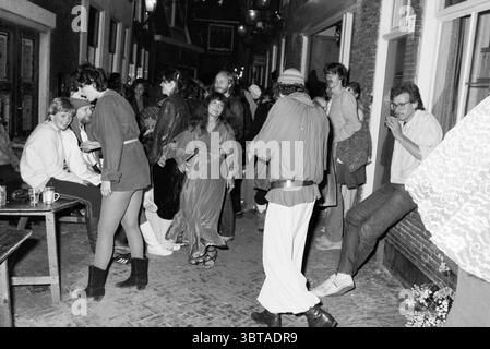 Medieval Feast of the Ark Festivties, Whizgle News, Dutch Desk, Niederlande, 1950 - 2000 am 28.05.1980. Dies sind die Themen im Bild. Die Szene zeigt eine lebhafte Zusammenkunft in einer engen, schwach beleuchteten Gasse, die eine intime, aber geschäftige Atmosphäre schafft. Die einzelnen Personen sind im Vordergrund verstreut, einige sind im Gespräch, andere scheinen zu tanzen oder ihre Umgebung zu genießen. Im Zentrum der Komposition schwingt eine Frau in einem fließenden, durchscheinenden Kleid anmutig und verkörpert den sorglosen Geist der Versammlung. In der Nähe umarmt ein Mann in lockerer Kleidung die Stockfoto