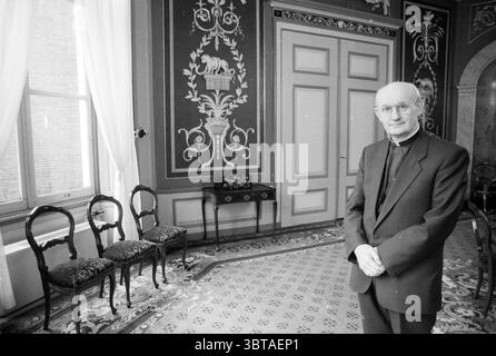 Bischof Bomers Roman Catholic Church, Whizgle News, Dutch Desk, Niederlande, 1950 - 2000 am 28.12.1988. Diese Themen sind in der Abbildung dargestellt. Die Szene fängt einen formellen Innenraum ein, der von eleganter Architektur und Einrichtung geprägt ist. Die Wände sind mit komplizierten Mustern verziert, mit detaillierten floralen und geometrischen Motiven in sanften, gedämpften Farben, die ein Gefühl klassischer Raffinesse hervorrufen. Natürliches Licht strömt durch ein großes Fenster, das mit transparenten Vorhängen bedeckt ist und sanfte Muster auf den gemusterten Boden wirft. Der Boden selbst besticht durch ein kunstvolles Design, das eine fesselnde visuelle Textur schafft Stockfoto