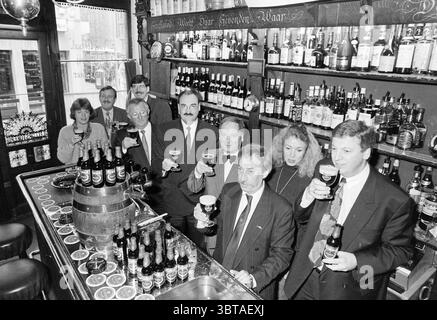 Präsentation von Silvester Beer, Whizgle News, Dutch Desk, Niederlande, 1950 - 2000 am 20-11-1991. Diese Themen werden in der Abbildung angezeigt. Die Szene fängt ein lebhaftes Treffen in einem schwach beleuchteten Pub mit nostalgischem Charme ein. Das Innere ist mit dunklen Holztäfelungen und Regalen ausgestattet, die bis zum Rand mit einer Reihe von Flaschen gefüllt sind, die jeweils einen anderen Geist widerspiegeln und zu der warmen, einladenden Atmosphäre beitragen. Im Vordergrund steht eine Gruppe von Individuen hinter einer polierten Bar, die jeweils ein Glas in einem feierlichen Toast hält. Ihre Ausdrücke reichen von fröhlichem Lächeln bis hin zu aufrichtigem l Stockfoto