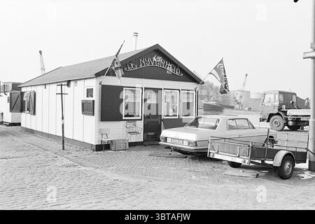 Koffiehuis De Nijverheid. Coffee, Whizgle News, Dutch Desk, Niederlande, 1950 - 2000 am 15-02-1978. Dies sind die Themen im Bild. Die Szene zeigt ein kleines, malerisches Gebäude, das sich durch seine Holzstruktur und das weiße Äußere auszeichnet. Die Fassade ist mit einem dekorativen Schild an der Oberseite verziert, das zu ihrem charmanten, rustikalen Charme beiträgt. Hervorzuheben sind zwei Flaggen, die wahrscheinlich verschiedene Betriebe oder Regionen repräsentieren und sanft im Wind flattern. Im Vordergrund steht ein Oldtimer neben einem Wohnwagen, der die nostalgische Atmosphäre noch verstärkt. Das Design des Fahrzeugs deutet auf eine längst vergangene Ära hin Stockfoto