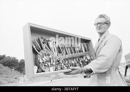 Ballpoint Collector Persons, Whizgle News, Dutch Desk, Niederlande, 1950 - 2000 am 26-05-1970. Diese Themen sind in der Abbildung dargestellt. In einer neutralen Umgebung steht eine Person prominent und hält eine große, offene Box, die bis zum Rand mit verschiedenen Werkzeugen und Instrumenten gefüllt ist. Die Box besteht aus glattem Holz, deren Oberfläche leicht unter weichem, diffusem Licht leuchtet. Das Sortiment an Objekten umfasst zahlreiche Schreibgeräte – Stifte, Bleistifte und Marker –, die in einer geordneten Anordnung angeordnet sind und eine Vielzahl von Farben und Größen aufweisen. Zu den Schreibwerkzeugen gehört eine Schere Stockfoto