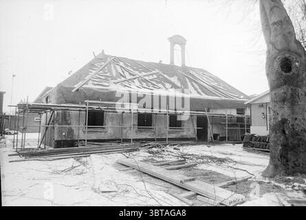 Restauration Schoten Rechthuis Restoration, Whizgle News, Dutch Desk, Niederlande, 1950 - 2000 am 04-01-1971. Diese Themen werden in der Abbildung angezeigt. Die Szene fängt ein teilweise gebautes Gebäude in einer einsamen Umgebung ein, die von einer winterlichen Atmosphäre geprägt ist. Das Gebäude, wahrscheinlich einst ein Wohnhaus oder ein Gemeinschaftsraum, verfügt über einen freiliegenden Dachrahmen mit Holzbalken, die gegen den grauen Himmel ragen. Die Wände befinden sich in verschiedenen Fertigungsphasen, wobei einige Bereiche freiliegende Dämmung aufweisen und andere eine raue, unbehandelte Oberfläche aufweisen. Um das Gebäude herum, Gerüste Stockfoto
