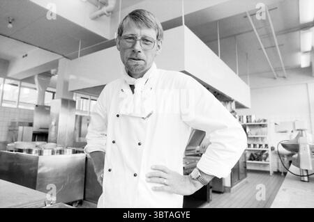 Koch Fred van Rijn Breezicht Altersheim IJmuiden Koken IJmuiden Niederlande, Whizgle News, Dutch Desk, Niederlande, 1950 - 2000 auf 30-06-1986. Die Abbildung zeigt diese Themen. In einer geräumigen Küche steht ein reifer Koch selbstbewusst mit einer Hand auf der Hüfte. Er hat einen nachdenklichen Ausdruck, verstärkt durch seine dünne Brille und seinen gepflegten Bart. Die Kleidung trägt einen traditionellen weißen Mantel des Küchenchefs und zeigt Knopfdetails, die sein professionelles Verhalten unterstreichen. Um ihn herum sind verschiedene Küchenelemente: Glänzende Edelstahlgeräte, große Töpfe und Pfannen, und gut Stockfoto