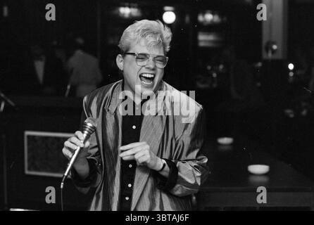 Sonstiges Künstler Gesangsfestival Zijlpoort Sing- und Gesangschöre Haarlem the Netherlands, Whizgle News, Dutch Desk, Niederlande, 1950 - 2000 am 24-04-1988. Diese Themen werden in der Abbildung angezeigt. In einem schwach beleuchteten Innenbereich ist die Szene voller Energie und Emotionen. Im Mittelpunkt der Komposition steht ein Individuum mit kurzen, hellen Haaren, die auf eine ganz besondere Art und Weise gestylt sind und Charisma ausstrahlen, während sie leidenschaftlich in ein Mikrofon singen. Ihr ausdrucksstarkes Gesicht, beleuchtet von weicher, diffuser Beleuchtung, zeigt ein breites, animiertes Lächeln, einen Moment purer Freude festhalten. Die Person trägt ein flimmerndes sil Stockfoto