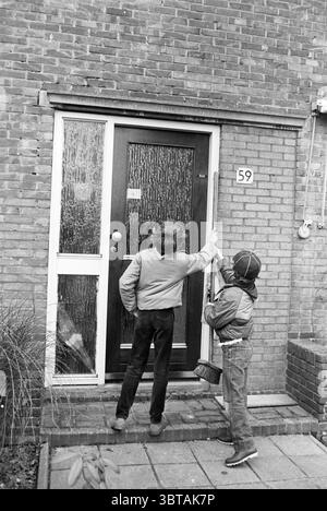 Junge Pfadfinder reinigen einen Park und Gehweg, Whizgle News, Dutch Desk, Niederlande, 1950 - 2000 am 11-04-1985. Dies sind die Elemente im Bild. In einer gedeckten, monochromen Umgebung stehen zwei Kinder vor einer Ziegelwand und sehen eine Tür. Die Ziegel haben einen tiefen Schatten, der der Szene Textur und Tiefe verleiht. Die Kinder, beide in für diese Zeit typischen Freizeitkleidung gekleidet, scheinen konzentriert zu sein. Ein Kind mit zerzausten Haaren und einer Jacke reicht zur Tür, während das andere, etwas kleiner und mit einer Mütze bekleidet, aufmerksam beobachtet. Die Tür selbst ist massiv und hölzerne, wie angestrichen Stockfoto