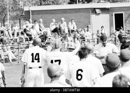 Baseball Kinheim - Neptunus, Whizgle News, Dutch Desk, Niederlande, 1950 - 2000 am 08-05-1993. Das Bild enthält diese Themen. Die Szene zeigt ein lebhaftes Baseballspiel in einem Outdoor-Stadion mit einem lebhaften grünen Feld. Die Spieler tragen klassische Sportuniformen, überwiegend weiß mit Kontrastfarben – ein Team zeigt Zahlen auf dem Rücken, während einige Kappen in Rot- und Schwarztönen tragen. Die Spieler sind in temperamentvollen Interaktionen involviert, einige heben ihre Arme und andere wirken kontemplativ. Im Hintergrund füllt eine Zuschauermenge den Bleichmacher Stockfoto