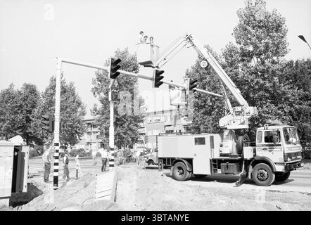 Installation von Ampeln Schipholweg Verkehrssicherheit Schipholweg, Whizgle News, Dutch Desk, Niederlande, 1950 - 2000 am 08-09-1988. Die Abbildung zeigt diese Themen. Die Szene erfasst eine geschäftige Kreuzung in der Stadt, an der ein Team mit der Wartung von Verkehrssignalen beschäftigt ist. Im Vordergrund ist ein großer Lkw strategisch positioniert und verfügt über einen markanten Arm, der bis zu den großen Ampeln verlängert ist. Dieses Fahrzeug hat ein robustes und zweckmäßiges Erscheinungsbild und ist in einer hellen Farbe lackiert, die einen Kontrast zur Umgebung bildet. Über dem Lkw befinden sich zwei Arbeiter in einer Schaufel, W Stockfoto
