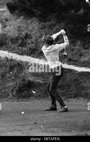Swing Golfer Golf Golf Golf Golf Golf, Whizgle News, Dutch Desk, Niederlande, 1950 - 2000 am 07-10-1986. Dies sind die Elemente im Bild. Die Szene fängt einen Golfer mitten im Schwung ein und zeigt eine dynamische Pose, die sowohl Konzentration als auch Energie vermittelt. Der Golfer trägt ein helles Langarmshirt in dunkler Hose, das dem Sport einen formellen und doch stylischen Touch verleiht. Seine Haare sind zerzaust, was auf eine luftige Umgebung im Freien hindeutet. Der Hintergrund zeigt eine üppige Grasfläche, gesäumt von wilden Grünflächen, die die natürliche Umgebung verbessern. Rechts, ein grasbewachsener Hang Stockfoto