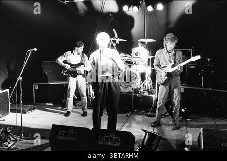 Rehearsal Pop-Gruppe Swing man Groups Rehearsal, Whizgle News, Dutch Desk, Niederlande, 1950 - 2000 am 15-08-1984. Die Abbildung zeigt diese Themen. Die Szene fängt eine dynamische Live-Musik-Performance auf einer schwach beleuchteten Bühne vor dunkler Kulisse ein. Die primäre Lichtquelle kommt von den Deckenstrahlern aus, die helle Lichtquellen auf die Darsteller werfen und dabei starke Schatten um sie herum erzeugen. Im Vordergrund steht ein Leadsänger, der in einem hellen, taillierten Hemd und einer dunklen Hose gekleidet ist. Seine ausdrucksstarke Haltung und seine Handgesten vermitteln ein Gefühl der Leidenschaft, während er sich engagiert Stockfoto